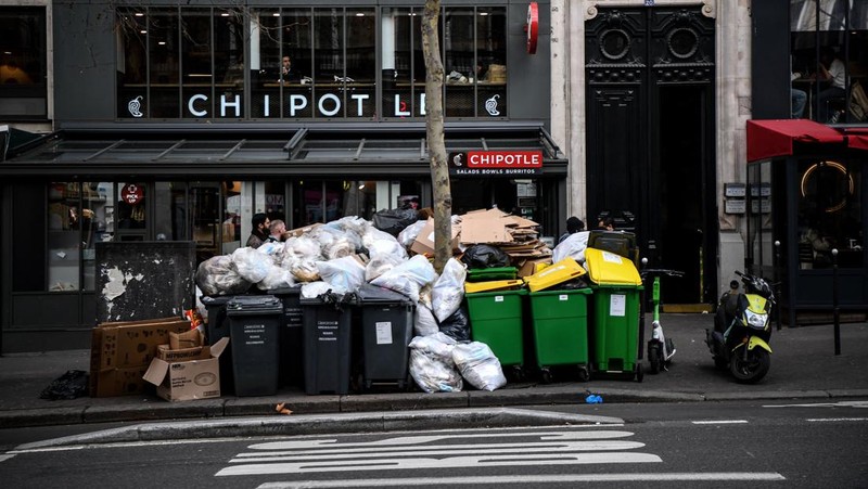 A worker walks past a pile of garbage bags that have been piling up since waste collectors went on strike against the French government's proposed pensions reform, in front of the Eiffel tower in Paris on March 15, 2023. - France faces another day of strikes on march 15, 2023, over highly contested pension reforms which President appears on the verge of pushing through despite months of protests. As the legislation enters the final stretch in parliament, trade unions are set to make another attempt to pressure the government and lawmakers into rejecting the proposed hike in the retirement age to 64. (Photo by Christophe ARCHAMBAULT / AFP) (Photo by CHRISTOPHE ARCHAMBAULT/AFP via Getty Images)