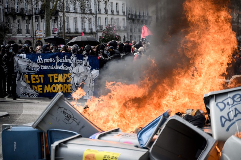 TOPSHOT - A protestor holds an umbrella to protect from teargas during a demonstration on the 8th day of strikes and protests across the country against the government's proposed pensions overhaul, in Nantes, on March 15, 2023. - France faces another day of strikes over highly contested pension reforms which President appears on the verge of pushing through despite months of protests. As the legislation enters the final stretch in parliament, trade unions are set to make another attempt to pressure the government and lawmakers into rejecting the proposed hike in the retirement age to 64. (Photo by LOIC VENANCE / AFP) (Photo by LOIC VENANCE/AFP via Getty Images)