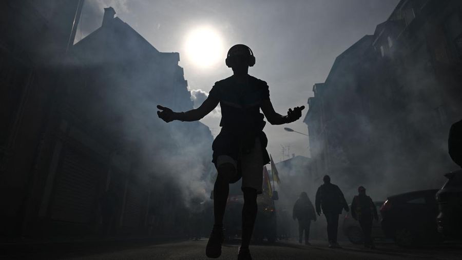 TOPSHOT - A protestor holds an umbrella to protect from teargas during a demonstration on the 8th day of strikes and protests across the country against the government's proposed pensions overhaul, in Nantes, on March 15, 2023. - France faces another day of strikes over highly contested pension reforms which President appears on the verge of pushing through despite months of protests. As the legislation enters the final stretch in parliament, trade unions are set to make another attempt to pressure the government and lawmakers into rejecting the proposed hike in the retirement age to 64. (Photo by LOIC VENANCE / AFP) (Photo by LOIC VENANCE/AFP via Getty Images)