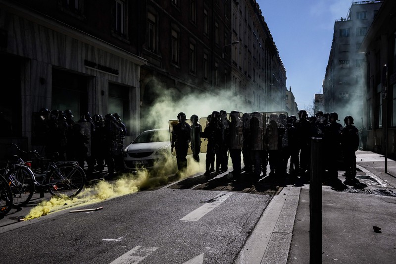 TOPSHOT - A protestor holds an umbrella to protect from teargas during a demonstration on the 8th day of strikes and protests across the country against the government's proposed pensions overhaul, in Nantes, on March 15, 2023. - France faces another day of strikes over highly contested pension reforms which President appears on the verge of pushing through despite months of protests. As the legislation enters the final stretch in parliament, trade unions are set to make another attempt to pressure the government and lawmakers into rejecting the proposed hike in the retirement age to 64. (Photo by LOIC VENANCE / AFP) (Photo by LOIC VENANCE/AFP via Getty Images)