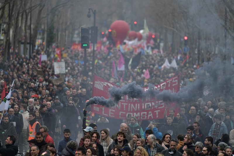 TOPSHOT - A protestor holds an umbrella to protect from teargas during a demonstration on the 8th day of strikes and protests across the country against the government's proposed pensions overhaul, in Nantes, on March 15, 2023. - France faces another day of strikes over highly contested pension reforms which President appears on the verge of pushing through despite months of protests. As the legislation enters the final stretch in parliament, trade unions are set to make another attempt to pressure the government and lawmakers into rejecting the proposed hike in the retirement age to 64. (Photo by LOIC VENANCE / AFP) (Photo by LOIC VENANCE/AFP via Getty Images)