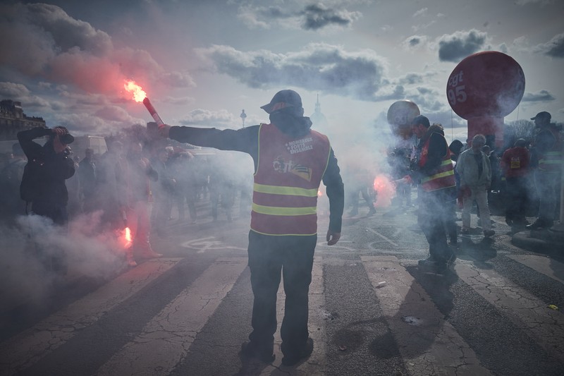 TOPSHOT - A protestor holds an umbrella to protect from teargas during a demonstration on the 8th day of strikes and protests across the country against the government's proposed pensions overhaul, in Nantes, on March 15, 2023. - France faces another day of strikes over highly contested pension reforms which President appears on the verge of pushing through despite months of protests. As the legislation enters the final stretch in parliament, trade unions are set to make another attempt to pressure the government and lawmakers into rejecting the proposed hike in the retirement age to 64. (Photo by LOIC VENANCE / AFP) (Photo by LOIC VENANCE/AFP via Getty Images)