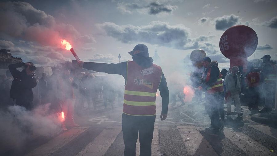 TOPSHOT - A protestor holds an umbrella to protect from teargas during a demonstration on the 8th day of strikes and protests across the country against the government's proposed pensions overhaul, in Nantes, on March 15, 2023. - France faces another day of strikes over highly contested pension reforms which President appears on the verge of pushing through despite months of protests. As the legislation enters the final stretch in parliament, trade unions are set to make another attempt to pressure the government and lawmakers into rejecting the proposed hike in the retirement age to 64. (Photo by LOIC VENANCE / AFP) (Photo by LOIC VENANCE/AFP via Getty Images)