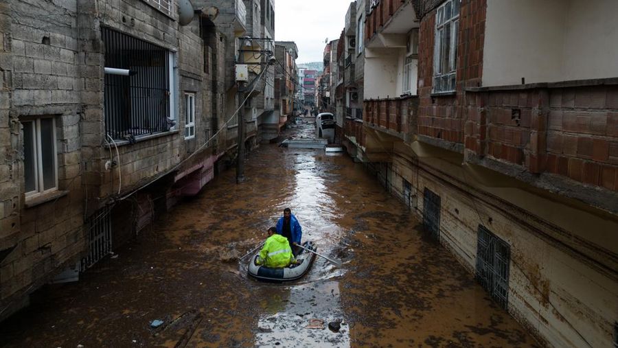 People stand at a high pont looking down at the flood waters in Sanliurfa, southeastern Turkey on March 15, 2023. - Flash floods killed at least 10 people living in tents and containers set up across Turkey's quake-hit southeast on March 15, 2023, according to media reports, with at least five people killed and another five missing in Adiyaman and Sanliurfa. (Photo by Demiroren News AAgency / DHA (Demiroren News Agency) / AFP) / - Turkey OUT / RESTRICTED TO EDITORIAL USE - MANDATORY CREDIT 