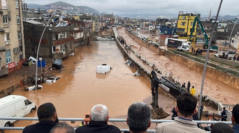 People stand at a high pont looking down at the flood waters in Sanliurfa, southeastern Turkey on March 15, 2023. - Flash floods killed at least 10 people living in tents and containers set up across Turkey's quake-hit southeast on March 15, 2023, according to media reports, with at least five people killed and another five missing in Adiyaman and Sanliurfa. (Photo by Demiroren News AAgency / DHA (Demiroren News Agency) / AFP) / - Turkey OUT / RESTRICTED TO EDITORIAL USE - MANDATORY CREDIT 