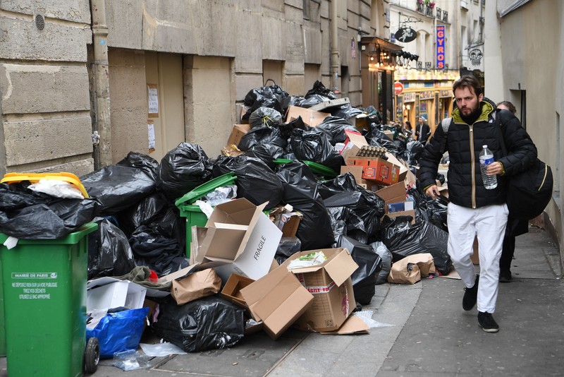 Pejalan kaki menutupi hidung mereka saat mereka berjalan melewati sampah yang berbau busuk di jalan saat para pemulung mogok menentang reformasi pensiun, di distrik 9 Paris pada 17 Maret 2023. Pejalan kaki menutupi hidung mereka saat mereka berjalan melewati sampah yang berbau busuk di jalan saat para pemulung mogok menentang reformasi pensiun, di distrik 9 Paris pada 17 Maret 2023. - Prancis memaksa pemulung sampah Paris untuk kembali bekerja setelah pemogokan selama berhari-hari menentang reformasi pensiun. Pekerja keluar dari pekerjaan sebagai protes terhadap rencana Presiden Emmanuel Macron untuk mereformasi sistem pensiun, dengan langkah-langkah utama menaikkan usia pensiun resmi menjadi 64 tahun dan meningkatkan jumlah tahun yang harus dibayar orang untuk menerima pensiun penuh. (BERTRAND GUAY/AFP via Getty Images)