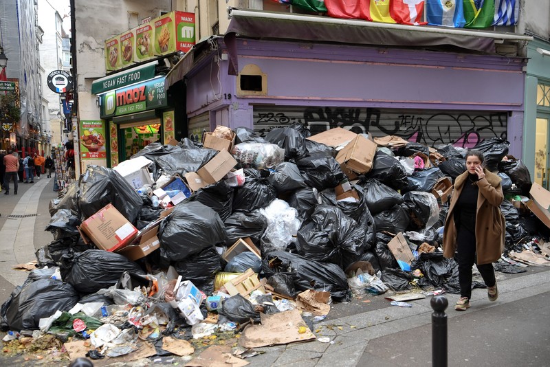 Pejalan kaki menutupi hidung mereka saat mereka berjalan melewati sampah yang berbau busuk di jalan saat para pemulung mogok menentang reformasi pensiun, di distrik 9 Paris pada 17 Maret 2023. - Prancis memaksa pemulung sampah Paris untuk kembali bekerja setelah pemogokan selama berhari-hari menentang reformasi pensiun. Pekerja keluar dari pekerjaan sebagai protes terhadap rencana Presiden Emmanuel Macron untuk mereformasi sistem pensiun, dengan langkah-langkah utama menaikkan usia pensiun resmi menjadi 64 tahun dan meningkatkan jumlah tahun yang harus dibayar orang untuk menerima pensiun penuh. (BERTRAND GUAY/AFP via Getty Images)
