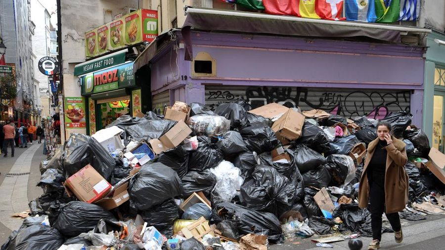 Pejalan kaki menutupi hidung mereka saat mereka berjalan melewati sampah yang berbau busuk di jalan saat para pemulung mogok menentang reformasi pensiun, di distrik 9 Paris pada 17 Maret 2023. - Prancis memaksa pemulung sampah Paris untuk kembali bekerja setelah pemogokan selama berhari-hari menentang reformasi pensiun. Pekerja keluar dari pekerjaan sebagai protes terhadap rencana Presiden Emmanuel Macron untuk mereformasi sistem pensiun, dengan langkah-langkah utama menaikkan usia pensiun resmi menjadi 64 tahun dan meningkatkan jumlah tahun yang harus dibayar orang untuk menerima pensiun penuh. (BERTRAND GUAY/AFP via Getty Images)