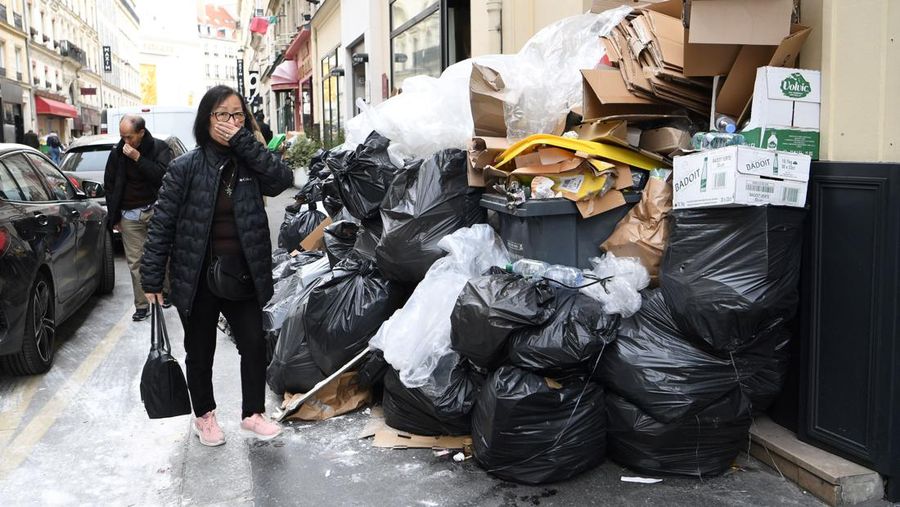 Pejalan kaki menutupi hidung mereka saat mereka berjalan melewati sampah yang berbau busuk di jalan saat para pemulung mogok menentang reformasi pensiun, di distrik 9 Paris pada 17 Maret 2023. - Prancis memaksa pemulung sampah Paris untuk kembali bekerja setelah pemogokan selama berhari-hari menentang reformasi pensiun. Pekerja keluar dari pekerjaan sebagai protes terhadap rencana Presiden Emmanuel Macron untuk mereformasi sistem pensiun, dengan langkah-langkah utama menaikkan usia pensiun resmi menjadi 64 tahun dan meningkatkan jumlah tahun yang harus dibayar orang untuk menerima pensiun penuh. (BERTRAND GUAY/AFP via Getty Images)