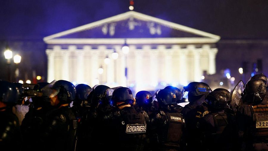 Seorang pengunjuk rasa memegang gambar Presiden Prancis Emmanuel Macron di dekat api selama demonstrasi di Place de la Concorde untuk memprotes penggunaan pasal 49.3 oleh pemerintah Prancis, klausul khusus dalam Konstitusi Prancis, untuk mendorong RUU reformasi pensiun melalui Majelis Nasional tanpa pemungutan suara oleh anggota parlemen, di Paris, Prancis, 17 Maret 2023. (REUTERS/Gonzalo Fuentes)