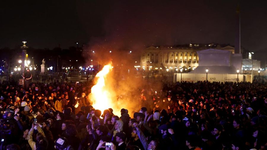 Seorang pengunjuk rasa memegang gambar Presiden Prancis Emmanuel Macron di dekat api selama demonstrasi di Place de la Concorde untuk memprotes penggunaan pasal 49.3 oleh pemerintah Prancis, klausul khusus dalam Konstitusi Prancis, untuk mendorong RUU reformasi pensiun melalui Majelis Nasional tanpa pemungutan suara oleh anggota parlemen, di Paris, Prancis, 17 Maret 2023. (REUTERS/Gonzalo Fuentes)