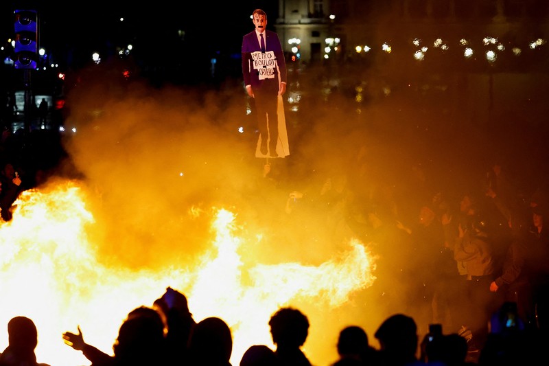 Seorang pengunjuk rasa memegang gambar Presiden Prancis Emmanuel Macron di dekat api selama demonstrasi di Place de la Concorde untuk memprotes penggunaan pasal 49.3 oleh pemerintah Prancis, klausul khusus dalam Konstitusi Prancis, untuk mendorong RUU reformasi pensiun melalui Majelis Nasional tanpa pemungutan suara oleh anggota parlemen, di Paris, Prancis, 17 Maret 2023. Seorang pengunjuk rasa memegang gambar Presiden Prancis Emmanuel Macron di dekat api selama demonstrasi di Place de la Concorde untuk memprotes penggunaan pasal 49.3 oleh pemerintah Prancis, klausul khusus dalam Konstitusi Prancis, untuk mendorong RUU reformasi pensiun melalui Majelis Nasional tanpa pemungutan suara oleh anggota parlemen, di Paris, Prancis, 17 Maret 2023. (REUTERS/Gonzalo Fuentes)