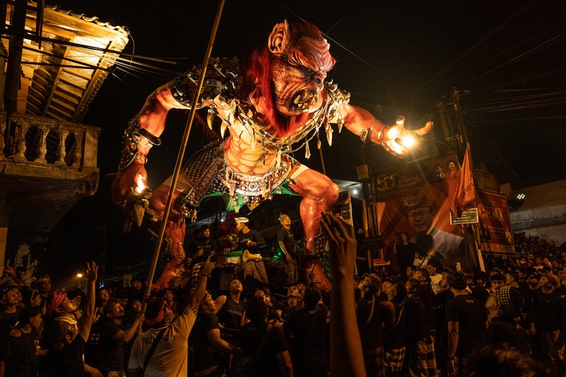 Pemuda Bali membawa ogoh-ogoh, boneka raksasa yang tampak mengancam saat pawai ogoh-ogoh pada malam Nyepi, Hari Raya Nyepi umat Hindu Bali yang menandai datangnya tahun baru Saka bulan pada 20 Maret 2023 di Tegalalang Desa, Gianyar, Bali, Indonesia. Umat Hindu di Bali melakukan serangkaian ritual pada awal Maret untuk merayakan tahun baru Imlek yang berpuncak pada perayaan Nyepi. Ogoh-ogoh menjadi salah satu pawai di awal tahun 1980-an. Sebelumnya, para peserta berkeliaran di jalan-jalan membawa obor bambu dan membuat suara keras dengan instrumen perkusi untuk menakut-nakuti setan. Di Bali masa kini, mayoritas ogoh-ogoh dibangun oleh anggota seka teruna teruni, sayap pemuda banjar. Nyepi berasal dari kata sepi atau sipeng yang artinya sepi, sepi, hening, nol, kosong, tidak ramai, tidak berisik, dan tidak ada aktivitas. Sejak tahun 1983, Nyepi menjadi hari libur nasional. Perayaan hari raya Nyepi bagi umat Hindu Bali di Indonesia merupakan kesempatan untuk refleksi diri yang disebut dengan mulat sarira. Semua penghuni dan pengunjung diwajibkan untuk mematuhi aturan yang disebut Catur Brata Penyepian, yang terdiri dari: tidak menyalakan api atau nyala api, tidak melakukan kegiatan yang menyenangkan, tidak bekerja atau bekerja, dan tidak melakukan perjalanan. (Agung Parameswara/Getty Images)