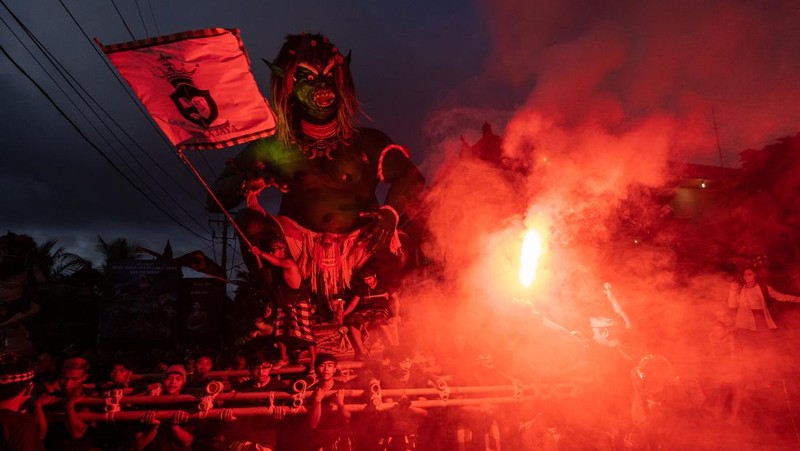 Pemuda Bali membawa ogoh-ogoh, boneka raksasa yang tampak mengancam saat pawai ogoh-ogoh pada malam Nyepi, Hari Raya Nyepi umat Hindu Bali yang menandai datangnya tahun baru Saka bulan pada 20 Maret 2023 di Tegalalang Desa, Gianyar, Bali, Indonesia. Umat Hindu di Bali melakukan serangkaian ritual pada awal Maret untuk merayakan tahun baru Imlek yang berpuncak pada perayaan Nyepi. Ogoh-ogoh menjadi salah satu pawai di awal tahun 1980-an. Sebelumnya, para peserta berkeliaran di jalan-jalan membawa obor bambu dan membuat suara keras dengan instrumen perkusi untuk menakut-nakuti setan. Di Bali masa kini, mayoritas ogoh-ogoh dibangun oleh anggota seka teruna teruni, sayap pemuda banjar. Nyepi berasal dari kata sepi atau sipeng yang artinya sepi, sepi, hening, nol, kosong, tidak ramai, tidak berisik, dan tidak ada aktivitas. Sejak tahun 1983, Nyepi menjadi hari libur nasional. Perayaan hari raya Nyepi bagi umat Hindu Bali di Indonesia merupakan kesempatan untuk refleksi diri yang disebut dengan mulat sarira. Semua penghuni dan pengunjung diwajibkan untuk mematuhi aturan yang disebut Catur Brata Penyepian, yang terdiri dari: tidak menyalakan api atau nyala api, tidak melakukan kegiatan yang menyenangkan, tidak bekerja atau bekerja, dan tidak melakukan perjalanan. (Agung Parameswara/Getty Images)