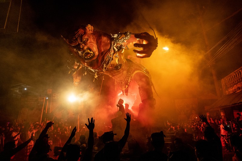 Pemuda Bali membawa ogoh-ogoh, boneka raksasa yang tampak mengancam saat pawai ogoh-ogoh pada malam Nyepi, Hari Raya Nyepi umat Hindu Bali yang menandai datangnya tahun baru Saka bulan pada 20 Maret 2023 di Tegalalang Desa, Gianyar, Bali, Indonesia. Umat Hindu di Bali melakukan serangkaian ritual pada awal Maret untuk merayakan tahun baru Imlek yang berpuncak pada perayaan Nyepi. Ogoh-ogoh menjadi salah satu pawai di awal tahun 1980-an. Sebelumnya, para peserta berkeliaran di jalan-jalan membawa obor bambu dan membuat suara keras dengan instrumen perkusi untuk menakut-nakuti setan. Di Bali masa kini, mayoritas ogoh-ogoh dibangun oleh anggota seka teruna teruni, sayap pemuda banjar. Nyepi berasal dari kata sepi atau sipeng yang artinya sepi, sepi, hening, nol, kosong, tidak ramai, tidak berisik, dan tidak ada aktivitas. Sejak tahun 1983, Nyepi menjadi hari libur nasional. Perayaan hari raya Nyepi bagi umat Hindu Bali di Indonesia merupakan kesempatan untuk refleksi diri yang disebut dengan mulat sarira. Semua penghuni dan pengunjung diwajibkan untuk mematuhi aturan yang disebut Catur Brata Penyepian, yang terdiri dari: tidak menyalakan api atau nyala api, tidak melakukan kegiatan yang menyenangkan, tidak bekerja atau bekerja, dan tidak melakukan perjalanan. (Agung Parameswara/Getty Images)