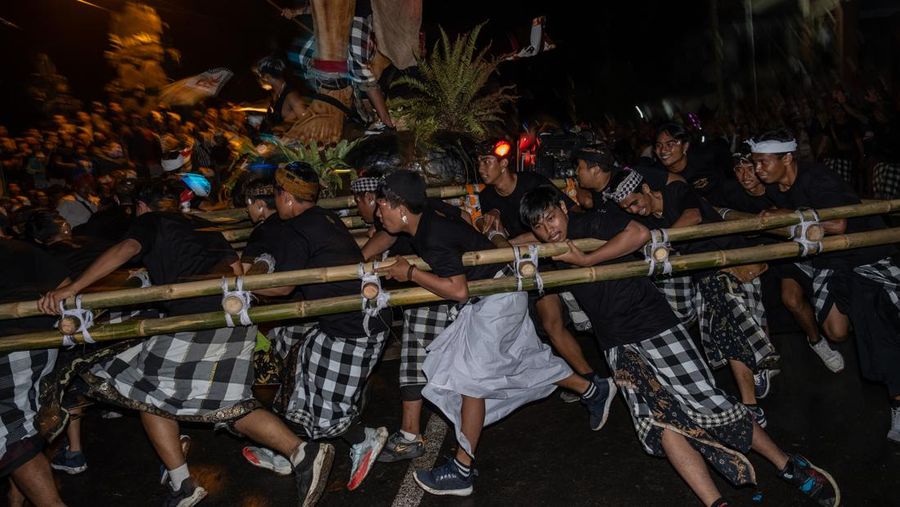 Pemuda Bali membawa ogoh-ogoh, boneka raksasa yang tampak mengancam saat pawai ogoh-ogoh pada malam Nyepi, Hari Raya Nyepi umat Hindu Bali yang menandai datangnya tahun baru Saka bulan pada 20 Maret 2023 di Tegalalang Desa, Gianyar, Bali, Indonesia. Umat Hindu di Bali melakukan serangkaian ritual pada awal Maret untuk merayakan tahun baru Imlek yang berpuncak pada perayaan Nyepi. Ogoh-ogoh menjadi salah satu pawai di awal tahun 1980-an. Sebelumnya, para peserta berkeliaran di jalan-jalan membawa obor bambu dan membuat suara keras dengan instrumen perkusi untuk menakut-nakuti setan. Di Bali masa kini, mayoritas ogoh-ogoh dibangun oleh anggota seka teruna teruni, sayap pemuda banjar. Nyepi berasal dari kata sepi atau sipeng yang artinya sepi, sepi, hening, nol, kosong, tidak ramai, tidak berisik, dan tidak ada aktivitas. Sejak tahun 1983, Nyepi menjadi hari libur nasional. Perayaan hari raya Nyepi bagi umat Hindu Bali di Indonesia merupakan kesempatan untuk refleksi diri yang disebut dengan mulat sarira. Semua penghuni dan pengunjung diwajibkan untuk mematuhi aturan yang disebut Catur Brata Penyepian, yang terdiri dari: tidak menyalakan api atau nyala api, tidak melakukan kegiatan yang menyenangkan, tidak bekerja atau bekerja, dan tidak melakukan perjalanan. (Agung Parameswara/Getty Images)