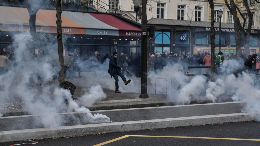 Protesters run in tear gas smoke next to   a street fire on the sidelines of a demonstration as part of a national day of strikes and protests, a week after the French government pushed a pensions reform through parliament without a vote, using the article 49.3 of the constitution, in Toulouse, southern France, on March 23, 2023. - French unions on March 23 staged a new day of disruption against the president's pension reform after he defiantly vowed to implement the change, which includes raising the age of retirement from 62 to 64, saying he was prepared to accept unpopularity in the face of sometimes violent protests. (Photo by Charly TRIBALLEAU / AFP)