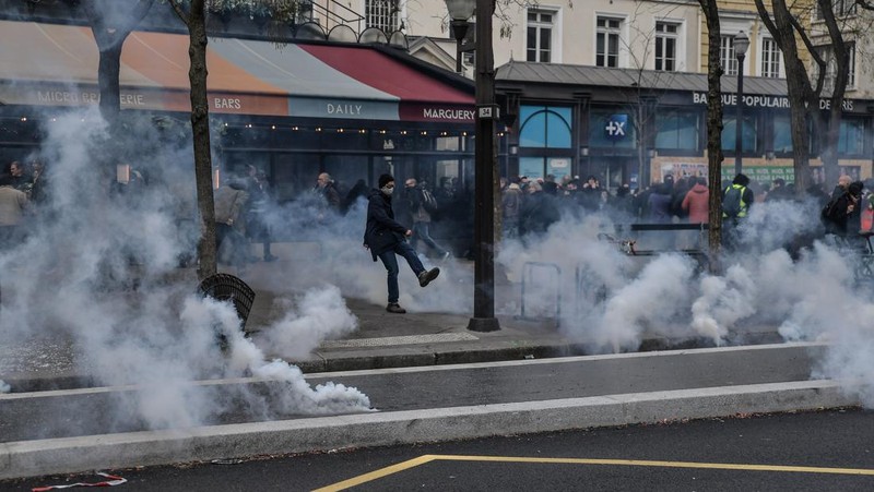 Protesters run in tear gas smoke next to   a street fire on the sidelines of a demonstration as part of a national day of strikes and protests, a week after the French government pushed a pensions reform through parliament without a vote, using the article 49.3 of the constitution, in Toulouse, southern France, on March 23, 2023. - French unions on March 23 staged a new day of disruption against the president's pension reform after he defiantly vowed to implement the change, which includes raising the age of retirement from 62 to 64, saying he was prepared to accept unpopularity in the face of sometimes violent protests. (Photo by Charly TRIBALLEAU / AFP)