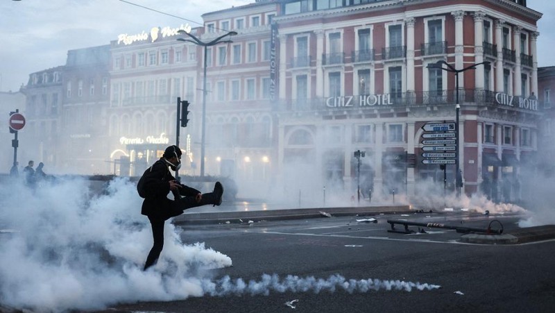 Protesters run in tear gas smoke next to   a street fire on the sidelines of a demonstration as part of a national day of strikes and protests, a week after the French government pushed a pensions reform through parliament without a vote, using the article 49.3 of the constitution, in Toulouse, southern France, on March 23, 2023. - French unions on March 23 staged a new day of disruption against the president's pension reform after he defiantly vowed to implement the change, which includes raising the age of retirement from 62 to 64, saying he was prepared to accept unpopularity in the face of sometimes violent protests. (Photo by Charly TRIBALLEAU / AFP)