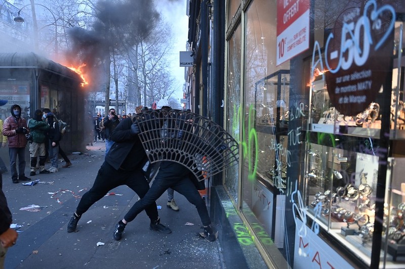 Protesters run in tear gas smoke next to   a street fire on the sidelines of a demonstration as part of a national day of strikes and protests, a week after the French government pushed a pensions reform through parliament without a vote, using the article 49.3 of the constitution, in Toulouse, southern France, on March 23, 2023. - French unions on March 23 staged a new day of disruption against the president's pension reform after he defiantly vowed to implement the change, which includes raising the age of retirement from 62 to 64, saying he was prepared to accept unpopularity in the face of sometimes violent protests. (Photo by Charly TRIBALLEAU / AFP)