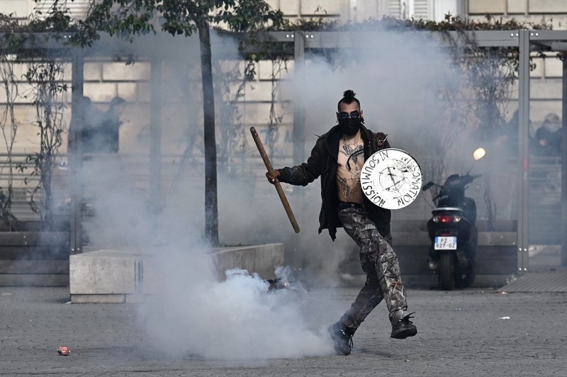 FRANCE-POLITICS-PENSIONS-DEMO Protesters run in tear gas smoke next to a street fire on the sidelines of a demonstration as part of a national day of strikes and protests, a week after the French government pushed a pensions reform through parliament without a vote, using the article 49.3 of the constitution, in Toulouse, southern France, on March 23, 2023. - French unions on March 23 staged a new day of disruption against the president's pension reform after he defiantly vowed to implement the change, which includes raising the age of retirement from 62 to 64, saying he was prepared to accept unpopularity in the face of sometimes violent protests. (Photo by Charly TRIBALLEAU / AFP)