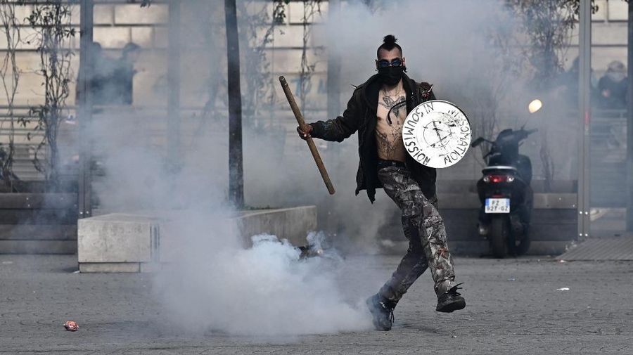 Protesters run in tear gas smoke next to   a street fire on the sidelines of a demonstration as part of a national day of strikes and protests, a week after the French government pushed a pensions reform through parliament without a vote, using the article 49.3 of the constitution, in Toulouse, southern France, on March 23, 2023. - French unions on March 23 staged a new day of disruption against the president's pension reform after he defiantly vowed to implement the change, which includes raising the age of retirement from 62 to 64, saying he was prepared to accept unpopularity in the face of sometimes violent protests. (Photo by Charly TRIBALLEAU / AFP)