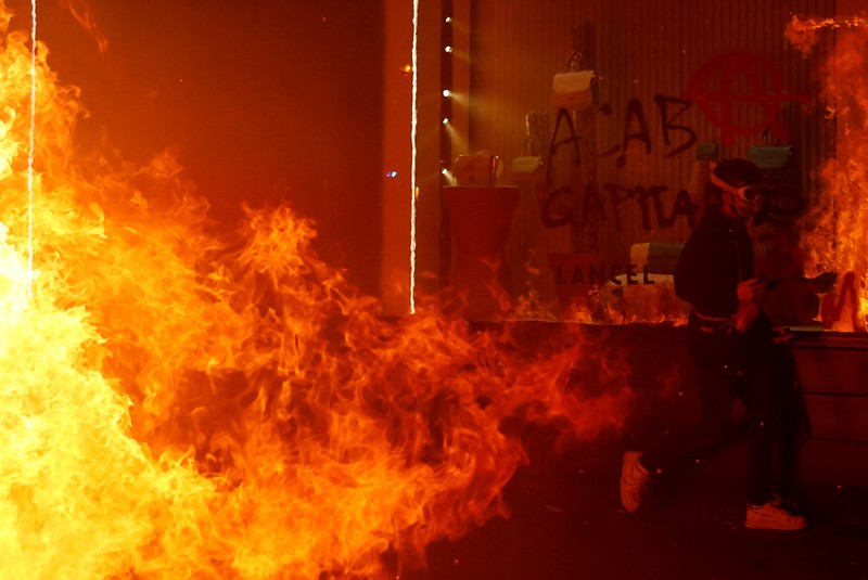 Seorang petugas polisi Prancis dengan pakaian anti huru hara berdiri di samping api selama demonstrasi di Bordeaux, Prancis (AFP via Getty Images/THIBAUD MORITZ)