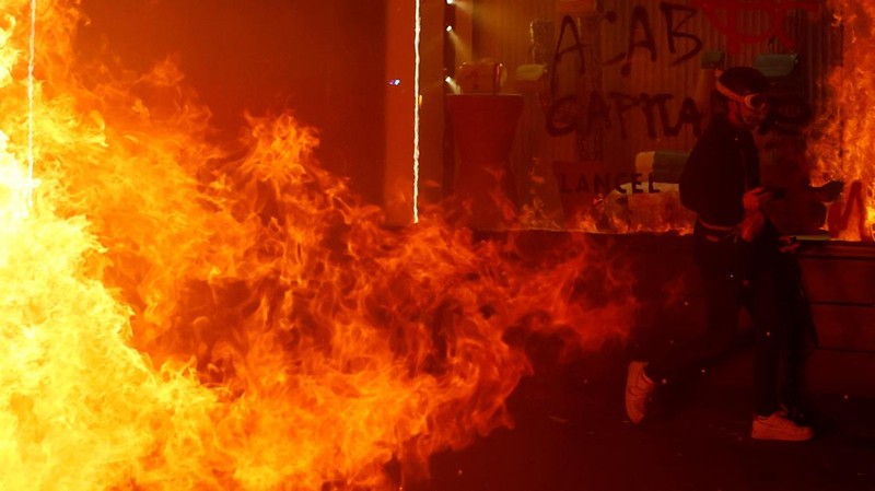 Seorang petugas polisi Prancis dengan pakaian anti huru hara berdiri di samping api selama demonstrasi di Bordeaux, Prancis (AFP via Getty Images/THIBAUD MORITZ)