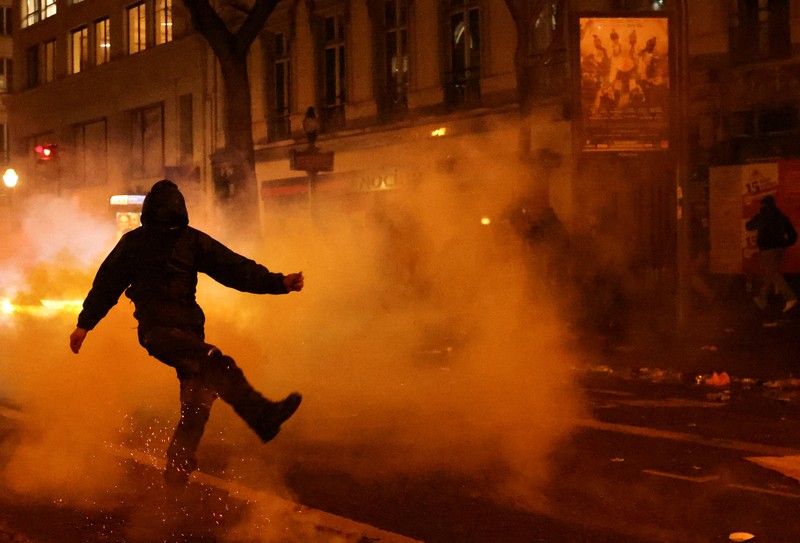 Seorang petugas polisi Prancis dengan pakaian anti huru hara berdiri di samping api selama demonstrasi di Bordeaux, Prancis (AFP via Getty Images/THIBAUD MORITZ)