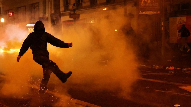 Seorang petugas polisi Prancis dengan pakaian anti huru hara berdiri di samping api selama demonstrasi di Bordeaux, Prancis (AFP via Getty Images/THIBAUD MORITZ)