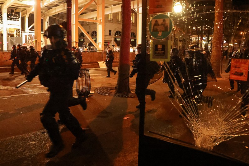 Seorang petugas polisi Prancis dengan pakaian anti huru hara berdiri di samping api selama demonstrasi di Bordeaux, Prancis (AFP via Getty Images/THIBAUD MORITZ)
