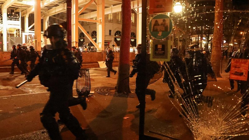 Seorang petugas polisi Prancis dengan pakaian anti huru hara berdiri di samping api selama demonstrasi di Bordeaux, Prancis (AFP via Getty Images/THIBAUD MORITZ)
