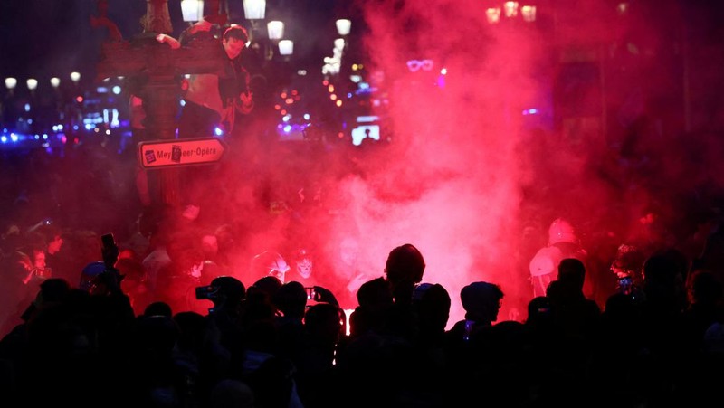 Seorang petugas polisi Prancis dengan pakaian anti huru hara berdiri di samping api selama demonstrasi di Bordeaux, Prancis (AFP via Getty Images/THIBAUD MORITZ)