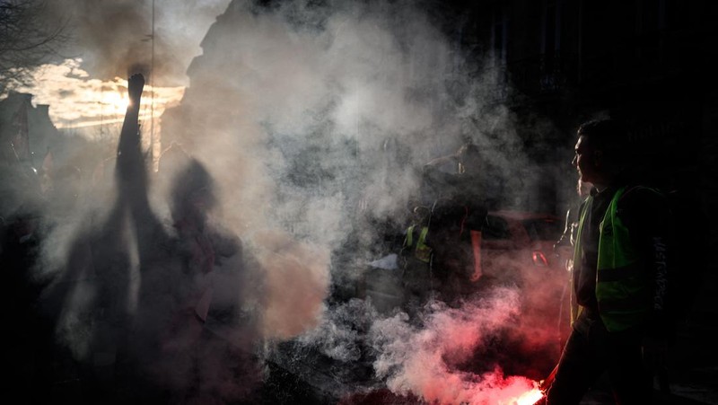 Seorang petugas polisi Prancis dengan pakaian anti huru hara berdiri di samping api selama demonstrasi di Bordeaux, Prancis (AFP via Getty Images/THIBAUD MORITZ)