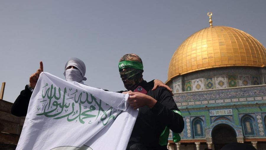 Para pria bertopeng mengangkat spanduk berlogo Brigade Ezzedine al-Qassam, sayap militer gerakan Hamas Palestina, setelah shalat Jumat pertama di bulan puasa Ramadhan, di depan kuil Dome of the Rock di Masjidil Haram. Kompleks masjid Al-Aqsa di Yerusalem, pada 24 Maret 2023. (AFP via Getty Images/AHMAD GHARABLI)