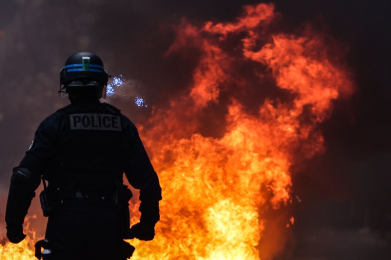 Seorang petugas polisi Prancis dengan pakaian anti huru hara berdiri di samping api selama demonstrasi di Bordeaux, Prancis (AFP via Getty Images/THIBAUD MORITZ) Seorang petugas polisi Prancis dengan pakaian anti huru hara berdiri di samping api selama demonstrasi di Bordeaux, Prancis (AFP via Getty Images/THIBAUD MORITZ)