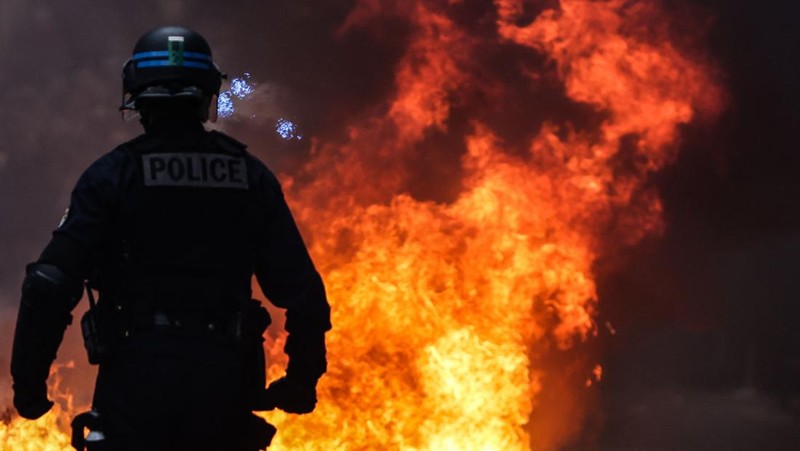 Seorang petugas polisi Prancis dengan pakaian anti huru hara berdiri di samping api selama demonstrasi di Bordeaux, Prancis (AFP via Getty Images/THIBAUD MORITZ)