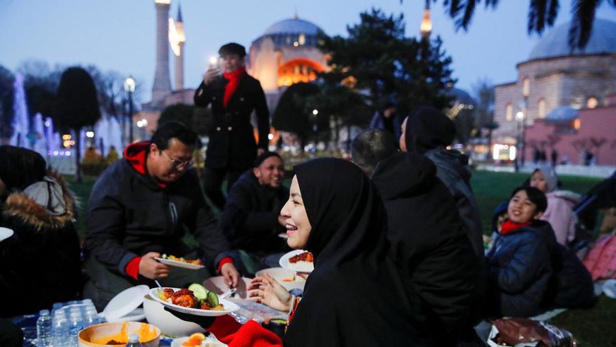 People, with the Ayasofya-i Kebir Camii or Hagia Sophia Grand Mosque in the background, have their iftar (breaking fast) meal at Sultanahmet Square during first day of the holy month of Ramadan in Istanbul, Turkey, March 23, 2023. REUTERS/Dilara Senkaya