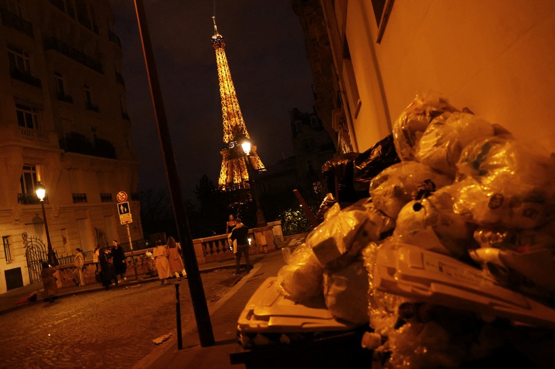 FRANCE-PENSIONS/GARBAGE Newlyweds Fabiana, 44, and Rob Burns, 53, from the U.S., pose for a photographer in front of overflowing garbage bins in a street near the Eiffel Tower as garbage has not been collected due to a strike of garbage collectors against the French government pension reform, in Paris, France, March 27, 2023. REUTERS/Nacho Doce TPX IMAGES OF THE DAY