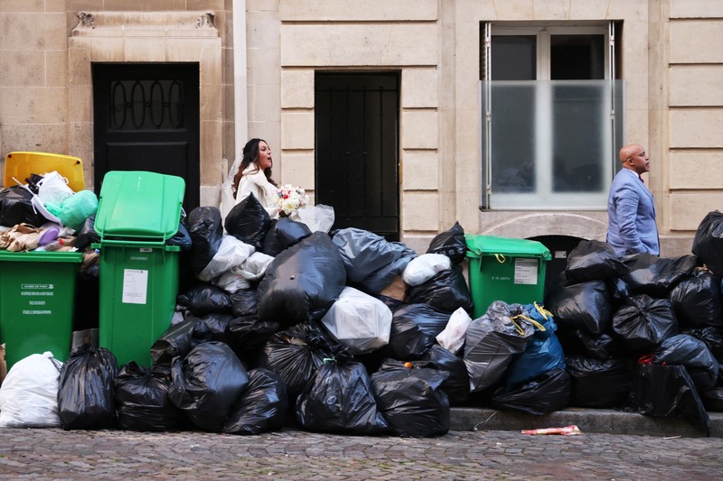 FRANCE-PENSIONS/GARBAGE Newlyweds Fabiana, 44, and Rob Burns, 53, from the U.S., pose for a photographer in front of overflowing garbage bins in a street near the Eiffel Tower as garbage has not been collected due to a strike of garbage collectors against the French government pension reform, in Paris, France, March 27, 2023. REUTERS/Nacho Doce TPX IMAGES OF THE DAY