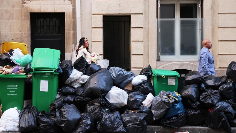 Newlyweds Fabiana, 44, and Rob Burns, 53, from the U.S., pose for a photographer in front of overflowing garbage bins in a street near the Eiffel Tower as garbage has not been collected due to a strike of garbage collectors against the French government pension reform, in Paris, France, March 27, 2023. REUTERS/Nacho Doce     TPX IMAGES OF THE DAY