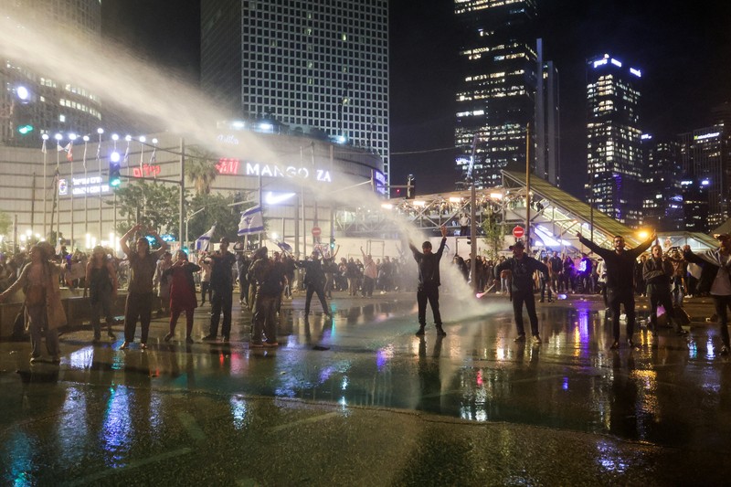 Israeli protesters react as a water cannon is used to disperse the people attending a demonstration against Israeli Prime Minister Benjamin Netanyahu and his nationalist coalition government's plan for judicial overhaul, in Tel Aviv, Israel, March 27, 2023. REUTERS/Itai Ron  NO RESALES. NO ARCHIVES