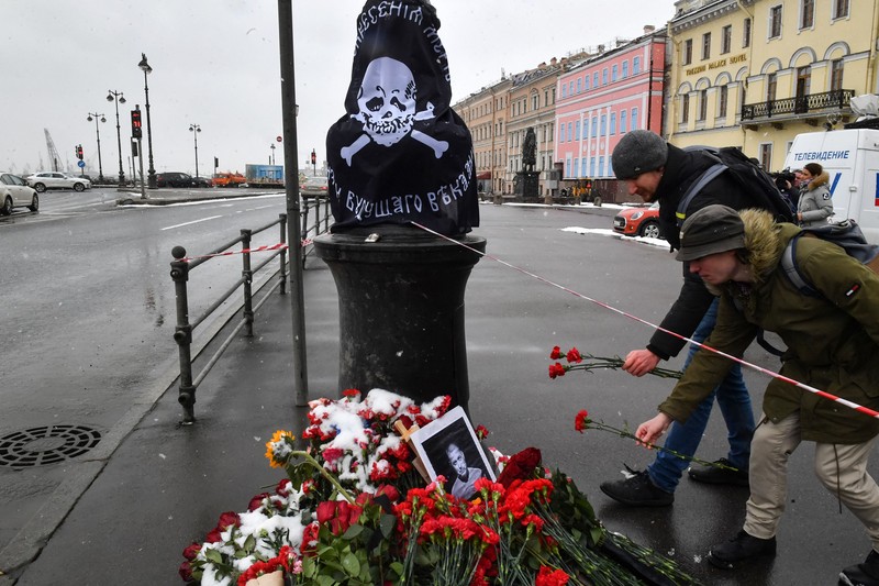 Para pria meletakkan bunga di tugu peringatan darurat untuk blogger militer Rusia Vladlen Tatarsky, yang bernama asli Maxim Fomin, yang tewas dalam ledakan bom 2 April di sebuah kafe, di lokasi ledakan di Saint Petersburg pada 3 April 2023. (OLGA MALTSEVA/AFP via Getty Images)