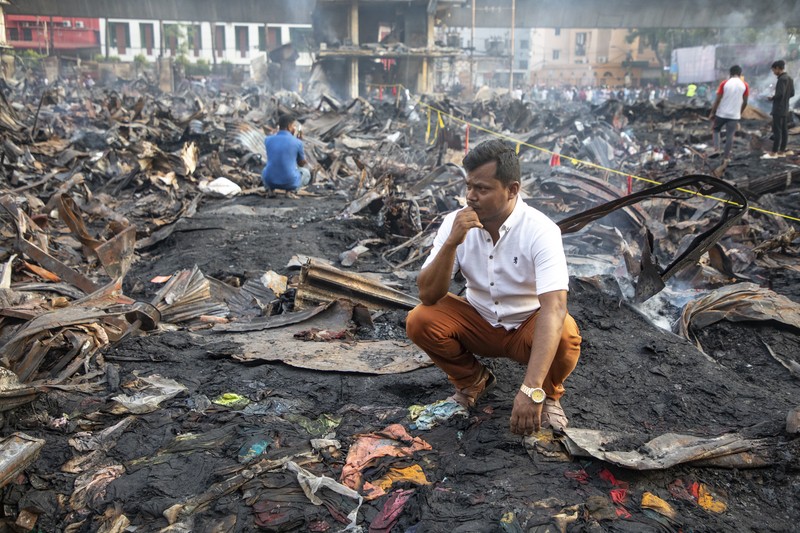 Pedagang korban kebakaran mencari barang dagangan, uang, dan barang berharga lainnya sementara asap terus mengepul dari reruntuhan yang hangus pada hari Rabu setelah kebakaran melanda kompleks perbelanjaan Bangabazar yang menampung beberapa ribu toko di Phulbariai Dhaka pada 05 April 2023. (Sony Ramany/NurPhoto via Getty Images)