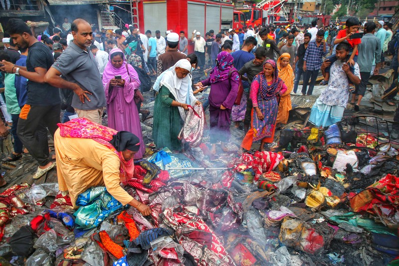 Pedagang korban kebakaran mencari barang dagangan, uang, dan barang berharga lainnya sementara asap terus mengepul dari reruntuhan yang hangus pada hari Rabu setelah kebakaran melanda kompleks perbelanjaan Bangabazar yang menampung beberapa ribu toko di Phulbariai Dhaka pada 05 April 2023. (Sony Ramany/NurPhoto via Getty Images)