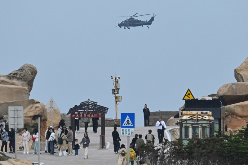 Helikopter militer China terbang melewati turis di titik pandang di atas Selat Taiwan, di pulau Pingtan, titik terdekat ke Taiwan, di provinsi Fujian tenggara China pada 7 April 2023. (GREG BAKER/AFP via Getty Images)