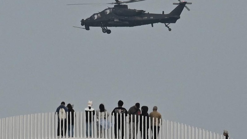 Helikopter militer China terbang melewati turis di titik pandang di atas Selat Taiwan, di pulau Pingtan, titik terdekat ke Taiwan, di provinsi Fujian tenggara China pada 7 April 2023. (GREG BAKER/AFP via Getty Images)