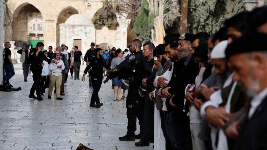 Pengunjung Yahudi berjalan melewati orang-orang yang membaca Alquran, di kompleks Masjid Al-Aqsa, yang dikenal umat Islam sebagai Tempat Suci Mulia dan bagi orang Yahudi sebagai Temple Mount, sementara ketegangan muncul selama bentrokan di Kota Tua Yerusalem, 9 April 2023. (REUTERS/Ammar Awad)