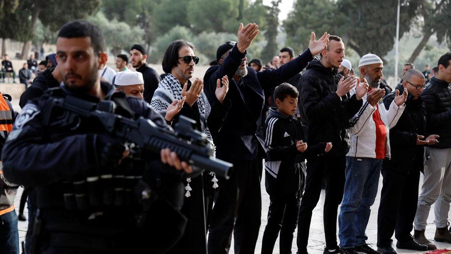 Pengunjung Yahudi berjalan melewati orang-orang yang membaca Alquran, di kompleks Masjid Al-Aqsa, yang dikenal umat Islam sebagai Tempat Suci Mulia dan bagi orang Yahudi sebagai Temple Mount, sementara ketegangan muncul selama bentrokan di Kota Tua Yerusalem, 9 April 2023. (REUTERS/Ammar Awad)