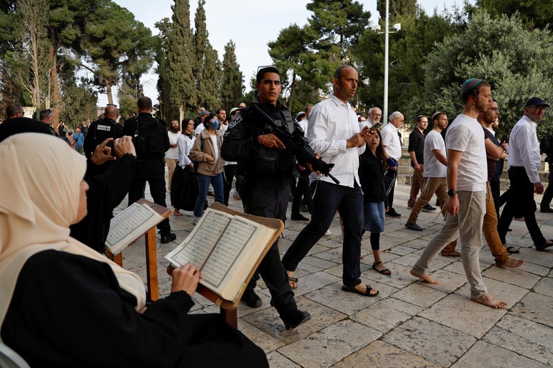 Pengunjung Yahudi berjalan melewati orang-orang yang membaca Alquran, di kompleks Masjid Al-Aqsa, yang dikenal umat Islam sebagai Tempat Suci Mulia dan bagi orang Yahudi sebagai Temple Mount, sementara ketegangan muncul selama bentrokan di Kota Tua Yerusalem, 9 April 2023. (REUTERS/Ammar Awad)